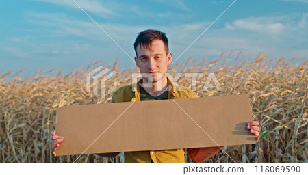 A man in a yellow shirt holds a blank cardboard sign while standing in a dry cornfield under a blue sky. A man in a yellow shirt holds a blank cardboard sign while standing in a dry cornfield under a blue sky. 118069590