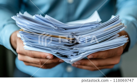 A person with a blue shirt holds a thick bundle of paperwork, indicating a busy day at the office. The setting is bright, reflecting a productive work atmosphere 118069747