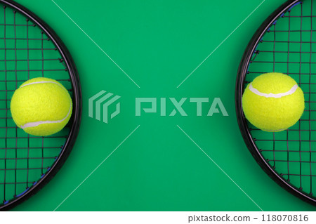Two black lawn tennis rackets lie on the sides on a green background, with a yellow tennis ball on top of them, with a place for text in the center. The concept of sports, games. High quality photo Two black lawn tennis rackets lie on the sides on a green background, with a yellow tennis ball on top of them, with a place for text in the center. The concept of sports, games. High quality photo 118070816