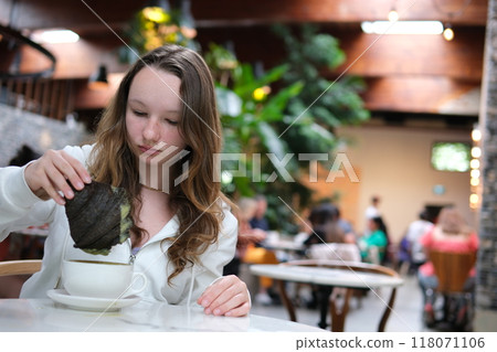 Girl in a cafe dips a Black Croissant into a cup of coffee 118071106