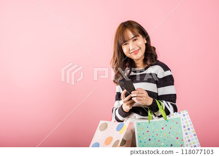 Portrait Asian happy beautiful young woman shopper smiling standing excited holding online shopping bags online multicolor and smartphone on hand, isolated on pink background, glad with mobile phone Portrait Asian happy beautiful young woman shopper smiling standing excited holding online shopping bags online multicolor and smartphone on hand, isolated on pink background, glad with mobile phone 118077103