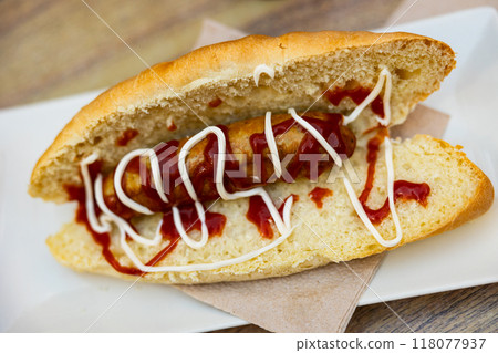 Sandwich from small fresh baguette with crispy crust stuffed with fried bratwurst sausage on plate  118077937