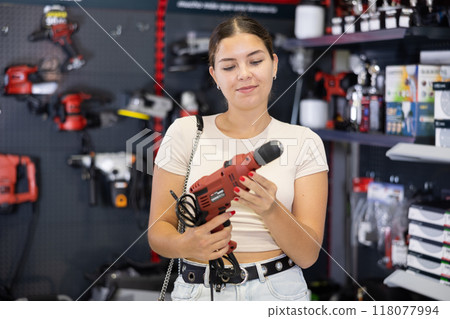 Smiling young woman choosing electric drill in hardware store Smiling young woman choosing electric drill in hardware store 118077994