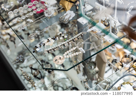Stylish ornaments for sale on glass shelves of bijouterie boutique Stylish ornaments for sale on glass shelves of bijouterie boutique 118077995