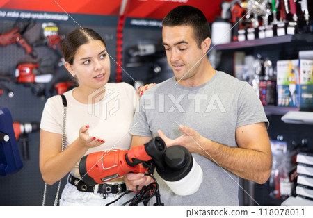 In store, spouses buyer doubts choice and closely examines electric paint-spraying machine spray gun 118078011