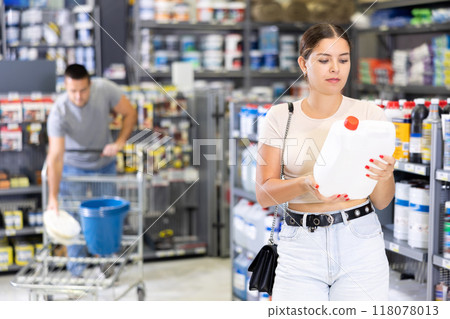 In store, woman hold plastic canister in hands and choice closely examines product 118078013
