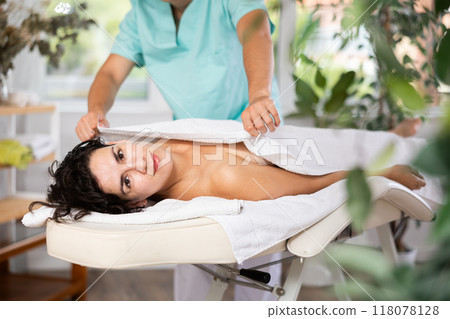 Male massage therapist carefully covers young relaxed woman with veil after massage 118078128
