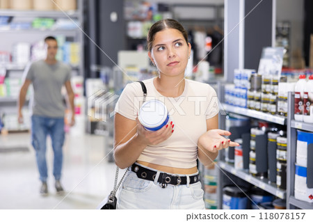 Woman buys paint tin in paintwork material store for carrying out internal finishing work on object 118078157