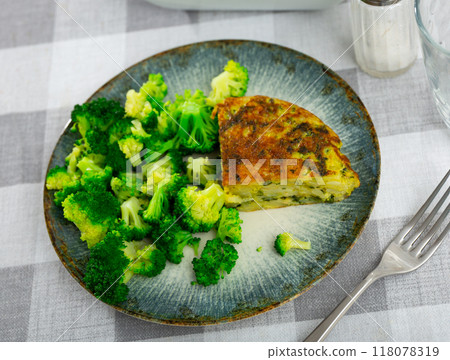 On plate is triangular piece of omelet with asparagus flecks, garnished with broccoli cabbage. 118078319
