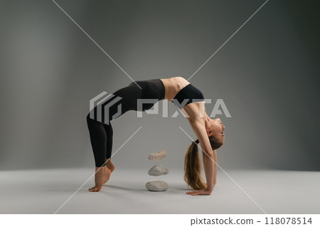A flexible individual performs a yoga pose with stones in the background 118078514