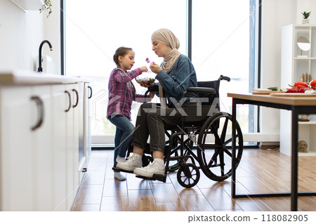Muslim mother in wheelchair and daughter sharing fresh salad in kitchen Muslim mother in wheelchair and daughter sharing fresh salad in kitchen 118082905