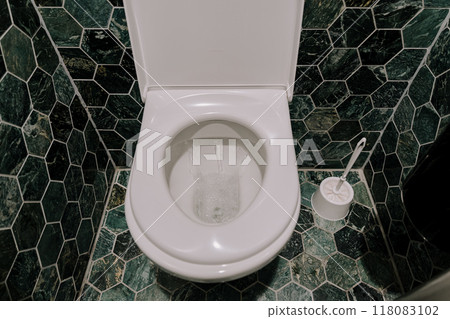 A toilet and toilet brush surrounded by a tiled wall A toilet and toilet brush surrounded by a tiled wall 118083102