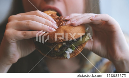 Close-up portrait of a woman in a fast food cafe eating a hamburger. Hungry woman eating a burger. 118083875