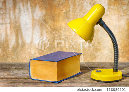 A table lamp and a book on old boards against a shabby background 118084201