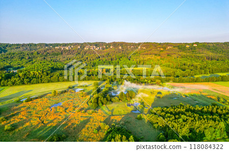 A breathtaking aerial view captures the Sedmihorky wetlands and Hruba Skala sandstone area in Bohemian Paradise, Czechia, showcasing lush greenery and mist in the serene morning light. 118084322