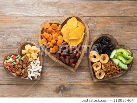 Healthy sweet dried fruits and berries in wooden heart shaped plates on wooden background.Top view. Healthy sweet dried fruits and berries in wooden heart shaped plates on wooden background.Top view. 118085404