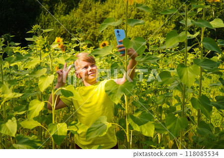 Carefree child with curly hair smiling and looking at camera while touching blooming flower on sunf 118085534