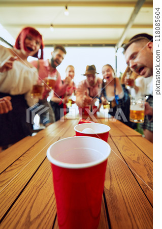 Group of people cheerfully playing beer pong, having fun and bar while celebrating beer festival. Bavarian traditions 118085604