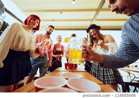 Focused and joyful faces, beer mugs in hand, Oktoberfest beer pong brings out competitive spirit, with fun and excitement in every throw 118085606