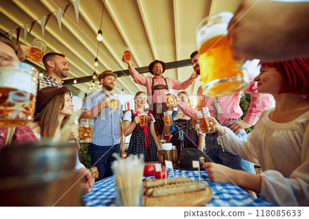 Men in traditional Bavarian clothes cheering group of his friends, people meeting at local pub for beer festival celebration 118085633