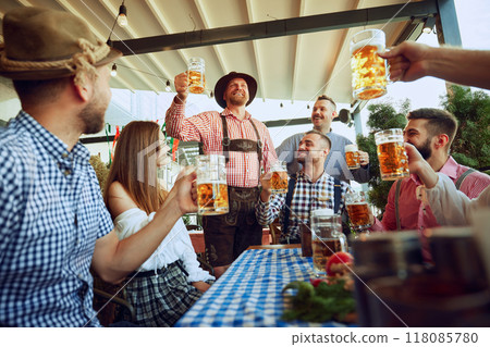 Group of friends, cheerful men and women raising beer mug in celebratory toast, having fun, leisure and enjoyment Group of friends, cheerful men and women raising beer mug in celebratory toast, having fun, leisure and enjoyment 118085780