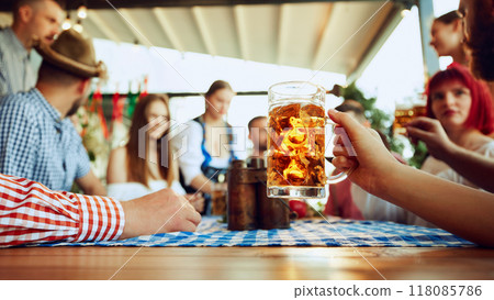 Focus on lager beer mug and blurred people, friends sitting at table at bar and celebrating, drinking, talking Focus on lager beer mug and blurred people, friends sitting at table at bar and celebrating, drinking, talking 118085786