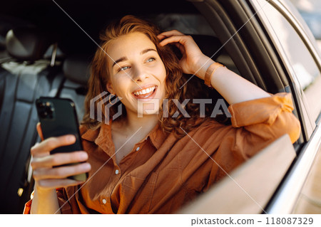 Smiling woman using smartphone while sitting in the back seat of a car. Business, technology concept Smiling woman using smartphone while sitting in the back seat of a car. Business, technology concept 118087329
