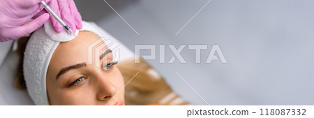 Close up of hands of young cosmetologist injecting botox in female face. She is standing and smiling. The woman is closed her eyes with relaxation 118087332