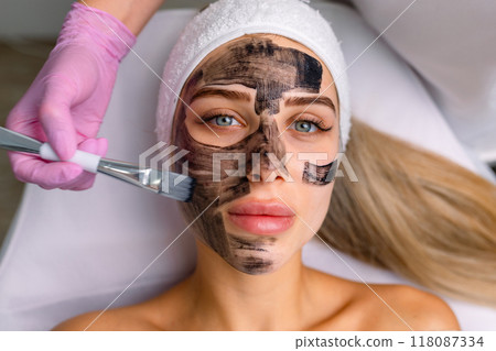 cosmetologist applying black mask on pretty woman face wearing black gloves, gorgeous woman in spa having facial procedures cosmetologist applying black mask on pretty woman face wearing black gloves, gorgeous woman in spa having facial procedures 118087334
