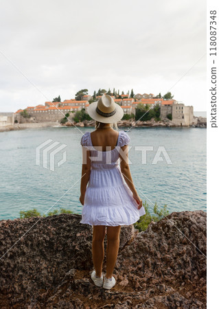 girl tourist in a hat looks from a top on the island of Sveti Stefan in Montenegro and the sea 118087348