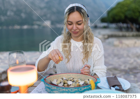A woman eats mussels, a traditional Montenegrin dish, while sitting on the terrace of a restaurant near the Bay of Kotor. Seafood and good summer vacation concept 118087375