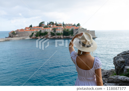 girl tourist in a hat looks from a top on the island of Sveti Stefan in Montenegro and the sea 118087377