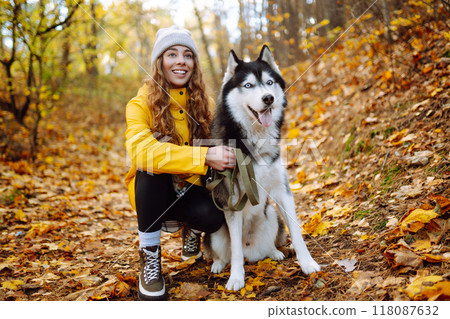 Beautiful young woman in a yellow coat walks in an autumn park with her pet husky. Beautiful young woman in a yellow coat walks in an autumn park with her pet husky. 118087632