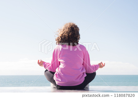 Person meditating on ledge by calm sea Person meditating on ledge by calm sea 118087820