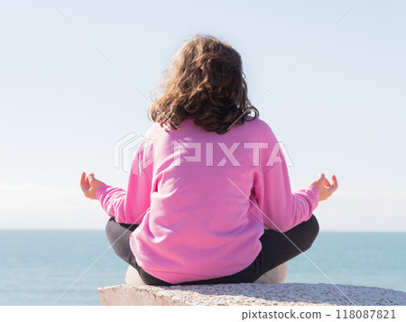 Person meditating on ledge by calm sea 118087821