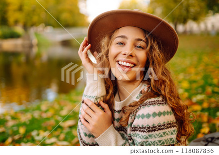 Happy woman in stylish sweater and hat outdoors in autumn park on plaid. Woman enjoys autumn nature. Happy woman in stylish sweater and hat outdoors in autumn park on plaid. Woman enjoys autumn nature. 118087836