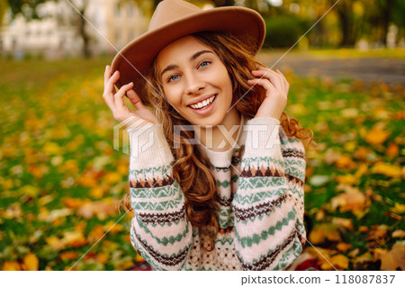 Happy woman in stylish sweater and hat outdoors in autumn park on plaid. Woman enjoys autumn nature. Happy woman in stylish sweater and hat outdoors in autumn park on plaid. Woman enjoys autumn nature. 118087837