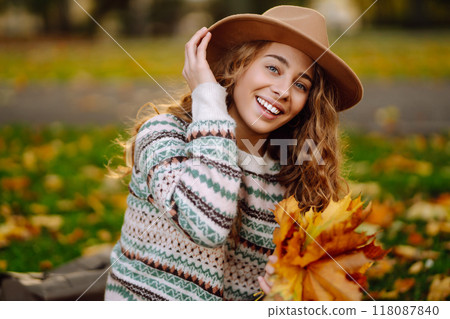Happy woman in stylish sweater and hat outdoors in autumn park on plaid. Woman enjoys autumn nature. 118087840