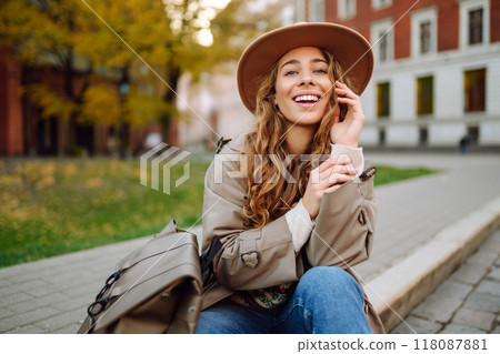 Smiling woman sitting posing against backdrop of streets of Europe, enjoying good autumn weather. 118087881