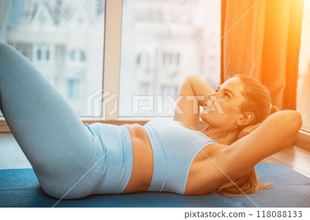 Young athletic attractive woman practicing yoga doing exercises. Works out at home or in a yoga studio, sportswear, blue pants and a full-length top indoors. Healthy lifestyle concept 118088133