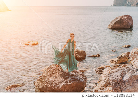 Woman green dress sea. Woman in a long mint dress posing on a beach with rocks on sunny day. Girl on the nature on blue sky background. 118088134
