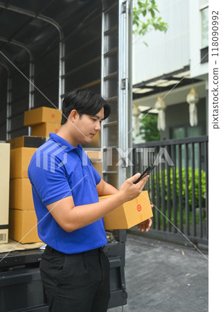 Young man courier holding cardboard box and using smartphone to confirm or manage deliveries Young man courier holding cardboard box and using smartphone to confirm or manage deliveries 118090992