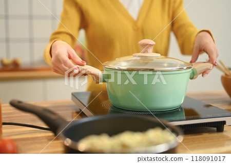 Close up shot of young woman is cooking in a green pot on a stove. People, food and domestic kitchen concept 118091017