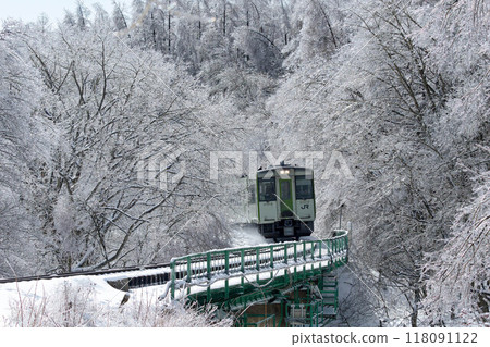 The Koumi Line Kiha 110 series train crosses an iron bridge through a forest of rain ice. 118091122