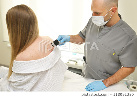 A dermatologist examines neoplasms on the patient's skin using a special dermatoscope device. Prevention of melanoma. A dermatologist examines neoplasms on the patient's skin using a special dermatoscope device. Prevention of melanoma. 118091380