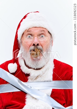 With pinecone in his mouth, Santa sits bound in duct tape, looking bewildered and motionless, his hands and feet securely taped to chair. 118092123