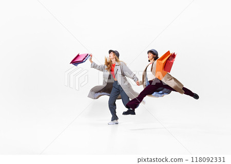 In motion to sales. Young beautiful women in stylish clothes energetically running with many hopping bags. Shopping journey. 118092331