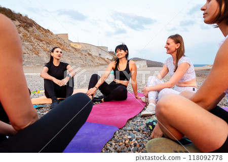 Close up bottom view of group of young-adult Caucasian women are sitting on sports mats and talking to each other. Concept of female circle of communication and outdoor yoga class Close up bottom view of group of young-adult Caucasian women are sitting on sports mats and talking to each other. Concept of female circle of communication and outdoor yoga class 118092778
