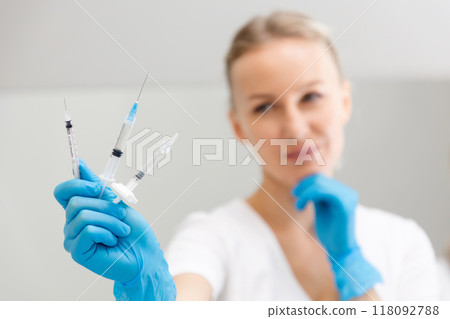 A blurry portrait of a cosmetologist woman holding three syringes in her hand. The concept of professional rejuvenating skin care A blurry portrait of a cosmetologist woman holding three syringes in her hand. The concept of professional rejuvenating skin care 118092788