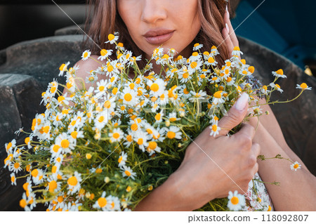 Summer time. A woman is holding a lush bouquet of daisies. In the background a tractor wheel. Close up portrait Summer time. A woman is holding a lush bouquet of daisies. In the background a tractor wheel. Close up portrait 118092807